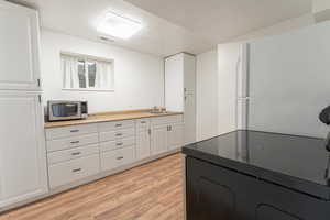 Kitchen featuring visible vents, stainless steel microwave, a sink, light wood-type flooring, and black electric range
