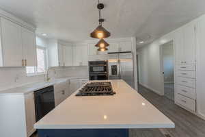 Kitchen with tasteful backsplash, stainless steel appliances, a center island, wood-style floors, and white cabinets