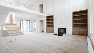 Unfurnished living room with built in shelves, stairway, a towering ceiling, and a healthy amount of sunlight