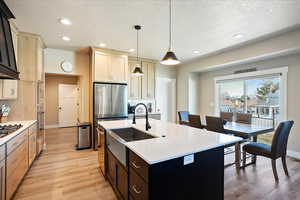 Kitchen with decorative light fixtures, a center island with sink, light wood finished floors, light countertops, and appliances with stainless steel finishes