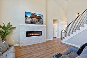 Living room with a stone fireplace, a high ceiling, wood finished floors, visible vents, and stairway