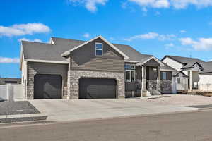 Craftsman-style house featuring concrete driveway, roof with shingles, stone siding, and fence