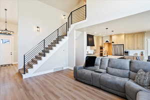 Living room with light wood-style flooring, a towering ceiling, visible vents, stairs, and baseboards