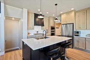 Kitchen featuring stainless steel appliances, light countertops, backsplash, a sink, and light wood-type flooring