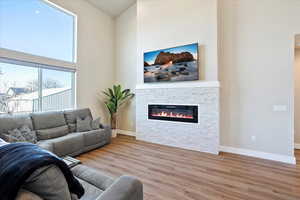 Living area featuring a high ceiling, baseboards, a fireplace, and wood finished floors