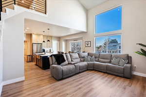 Living room featuring light wood-style floors, stairway, a towering ceiling, and baseboards