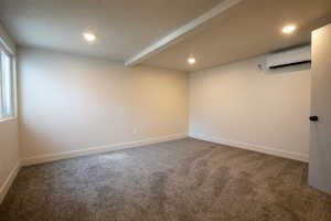 Carpeted spare room featuring a textured ceiling, an AC wall unit, recessed lighting, and baseboards