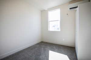 Empty room featuring baseboards, dark colored carpet, and an AC wall unit