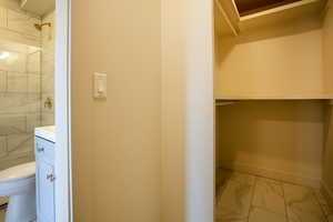 Bathroom featuring baseboards, toilet, marble finish floor, a tile shower, and vanity