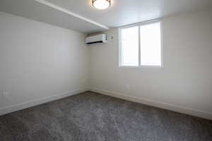 Spare room featuring dark colored carpet, a wall mounted air conditioner, a textured ceiling, and baseboards