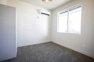 Unfurnished room with dark colored carpet, a wall mounted AC, and baseboards