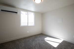 Carpeted spare room featuring a textured ceiling, baseboards, and an AC wall unit