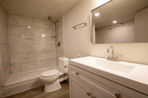 Full bathroom with toilet, a tile shower, wood finished floors, and vanity