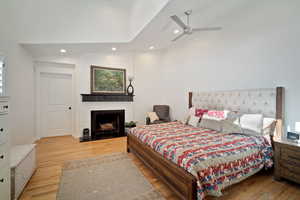 Bedroom featuring a ceiling fan, lofted ceiling, wood finished floors, a fireplace, and recessed lighting