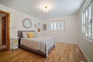 Bedroom featuring multiple windows, a notable chandelier, light wood-style flooring, and baseboards