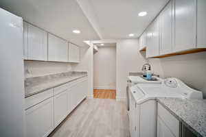 Clothes washing area featuring light wood-style flooring, recessed lighting, baseboards, washer and dryer, and cabinet space