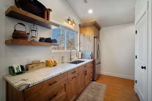 Kitchen with light stone counters, a sink, baseboards, stainless steel fridge with ice dispenser, and open shelves