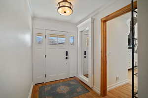 Entryway with ornamental molding, light wood-style flooring, and baseboards