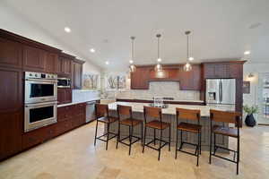 Kitchen with a large island, hanging light fixtures, decorative backsplash, appliances with stainless steel finishes, and vaulted ceiling