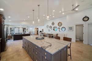 Kitchen with a breakfast bar area, a kitchen island, open floor plan, freestanding refrigerator, and light stone countertops