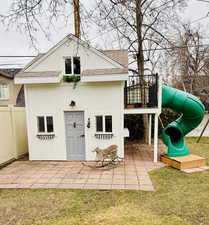 Rear view of house with a shingled roof, a lawn, a patio, fence, and a playground