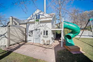 Rear view of property featuring fence, a lawn, a playground, and a patio