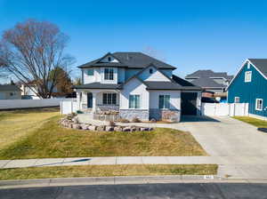 View of front facade featuring concrete driveway, stone siding, a gate, fence, and a front yard