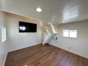 Unfurnished living room featuring a textured ceiling, a wall unit AC, wood finished floors, baseboards, and stairs