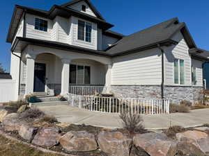 View of front of home featuring covered porch, stone siding, and roof with shingles