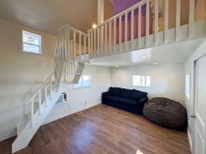 Living room with a textured ceiling, wood finished floors, a wall mounted air conditioner, baseboards, and stairs