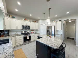 Kitchen featuring arched walkways, white cabinetry, appliances with stainless steel finishes, backsplash, and a center island