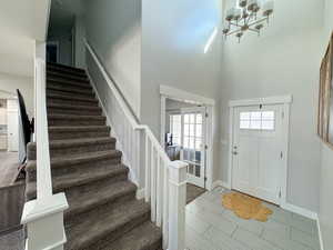 Foyer with a towering ceiling, stairway, baseboards, and an inviting chandelier