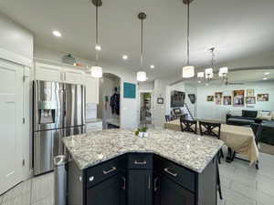 Kitchen featuring arched walkways, stainless steel fridge with ice dispenser, a center island, white cabinetry, and backsplash