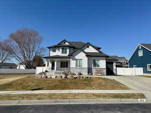 View of front facade featuring covered porch, fence, concrete driveway, stone siding, and a gate