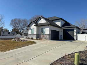 View of front of house featuring a garage, driveway, a shingled roof, stone siding, and fence