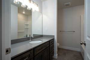 Bathroom with toilet, vanity, visible vents, and baseboards