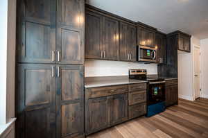 Kitchen featuring dark brown cabinetry, wood finished floors, stainless steel appliances, a textured ceiling, and light countertops