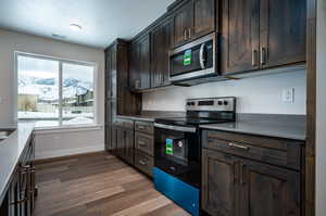 Kitchen with dark wood-style floors, range with electric stovetop, stainless steel microwave, visible vents, and dark brown cabinets