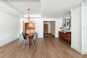 Dining room with light wood-type flooring, baseboards, a tray ceiling, and crown molding