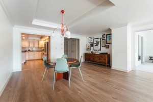 Dining room featuring baseboards, a tray ceiling, light wood-style flooring, and crown molding