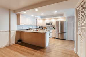 Kitchen with a peninsula, appliances with stainless steel finishes, light wood finished floors, a raised ceiling, and tasteful backsplash