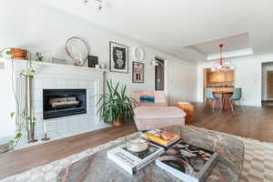 Living area with a tray ceiling, crown molding, wood finished floors, a tile fireplace, and baseboards