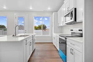 Kitchen with appliances with stainless steel finishes, white cabinetry, light stone countertops, light wood finished floors, and an island with sink