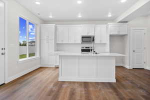 Kitchen with white cabinets, stainless steel microwave, light wood-style flooring, range with electric stovetop, and a kitchen island with sink