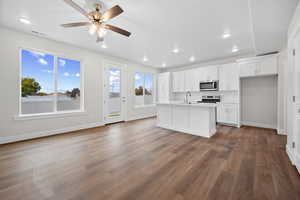 Kitchen with white cabinetry, stainless steel microwave, dark wood finished floors, a center island with sink, and recessed lighting