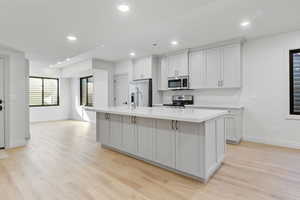 Kitchen featuring light quartzite countertops, appliances with stainless steel finishes, a galley island with built in sink, and recessed lighting