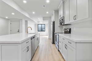 Kitchen featuring light wood finished floors, stainless steel appliances, white cabinetry and a galley island with built in sink.
