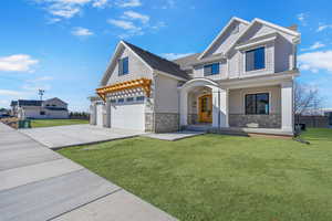 View of front of house with an attached garage, concrete driveway, a front lawn, and stone siding
