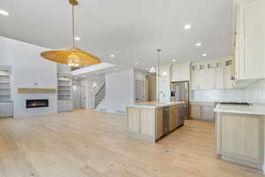 Kitchen featuring stainless steel appliances, light hardwood flooring, Galley island, tiled backsplash and quartzite countertops.
