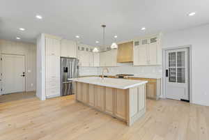 Kitchen featuring stainless steel appliances, premium range hood, light hardwood flooring, Galley island, tiled backsplash and quartzite countertops.
